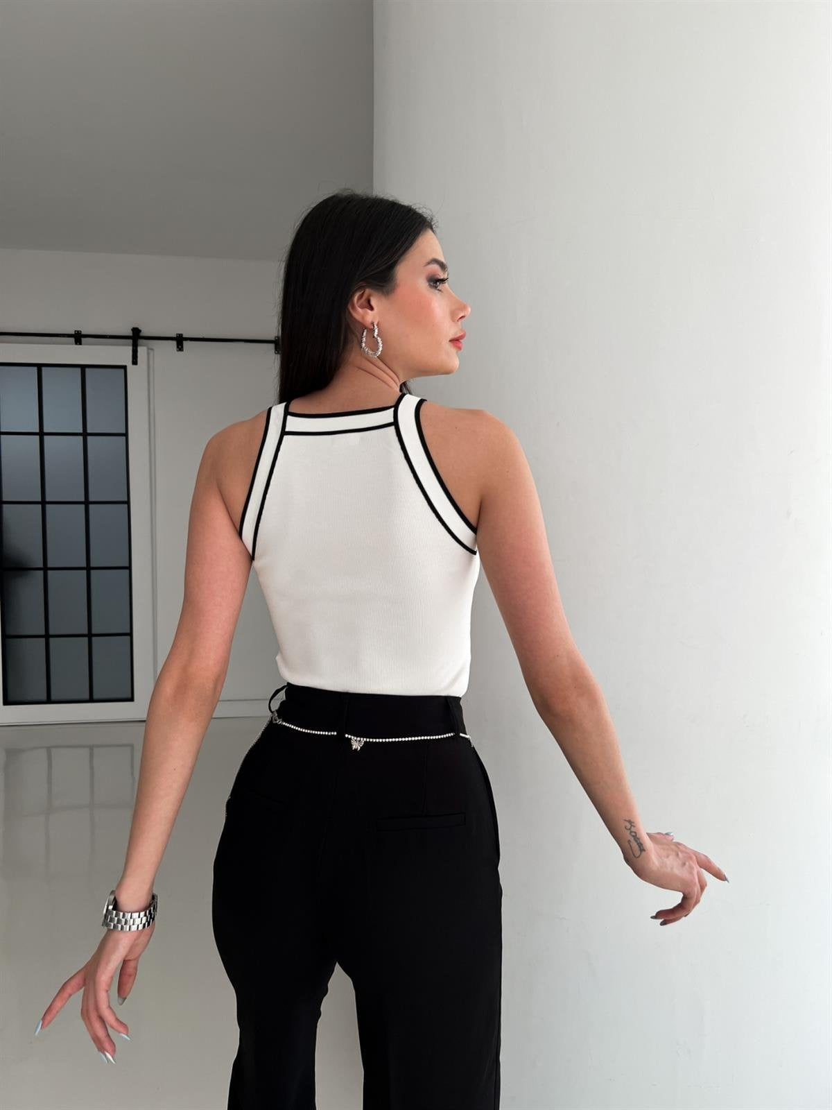 Top sin mangas en tono vainilla con detalles negros en el escote y los hombros; diseño 100% acrílico que complementa cualquier outfit