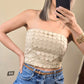 Imagen de plano medio de mujer con cabello color rubio vistiendo un statement piece (en forma de tubo) con diseño calado (circulos) en color beige tipo crop y un mahón azul high waist.  frente a un fondo neutral.