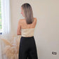 Imagen de espalda de mujer con cabello color rubio mostrando la parte trasera de un statement piece (en forma de tubo) con diseño calado (circulos) en color beige tipo crop y elasticos con cierre de zipper.   y un pantalón negro estructurado.  frente a un fondo neutral.