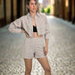 Mujer rubia con un set de camisa manga larga y botones frontales y un pantalon corto con diseño en color crema claro.