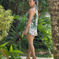 Mujer de espalda vistiedo un romper halter floreado color verde y beige con diseño cutout en el frente frente a unos jardines naturales.
