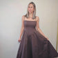Imagen de mujer luciendo un vestido largo color brown.  Con manguillos tipo espagueti y diseño que afina la cintura con una amplia falda que da movimiento.