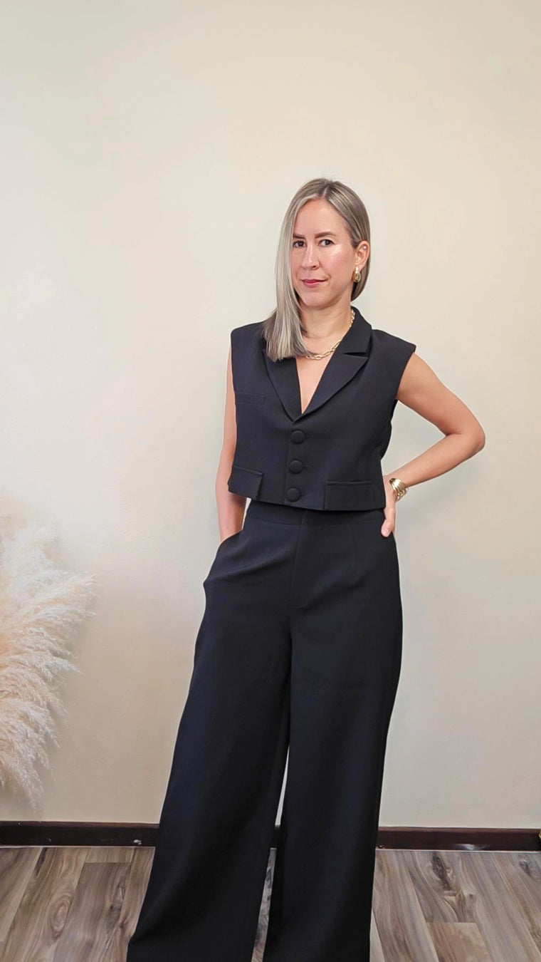 Imagen de mujer con cabello color rubio visitiendo un set de vest sin manga con botones frontales y pantalon a juego en color negro frente a un fondo neutro.  Este set es una pieza premium de la coleccion de new arrivals de la boutique Enso Amara.